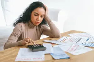 Pessoa calculando dívidas e analisando contas e faturas bancárias enquanto tenta entender o aumento da dívida bancária e os juros aplicados.